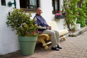 Ein Senior sitzt auf einer Gartenbank vor dem Seniorenpflegeheim Birkenhof in Erharting.